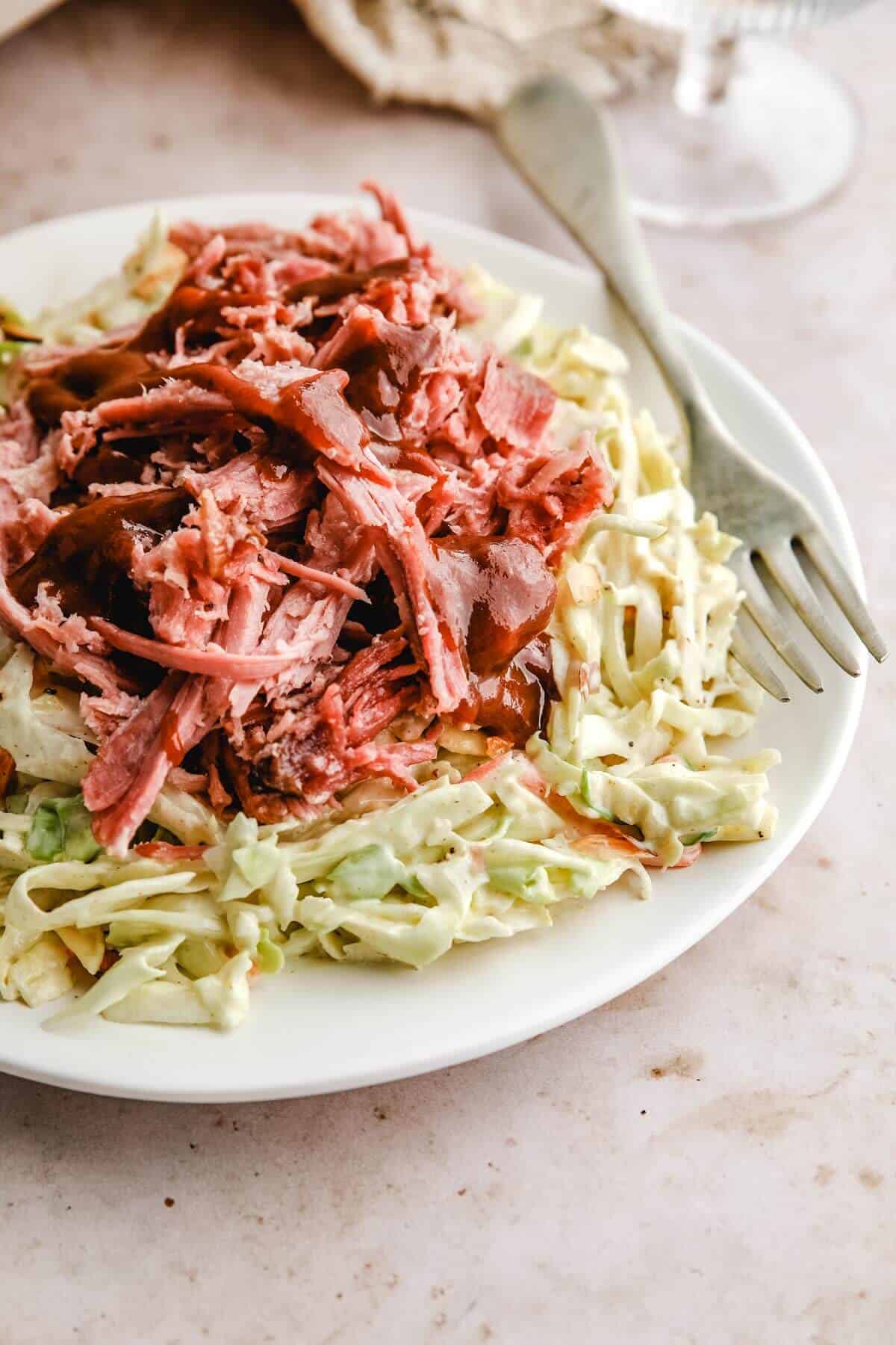 curry coleslaw on a plate with shredded pork and BBQ sauce over the top. 