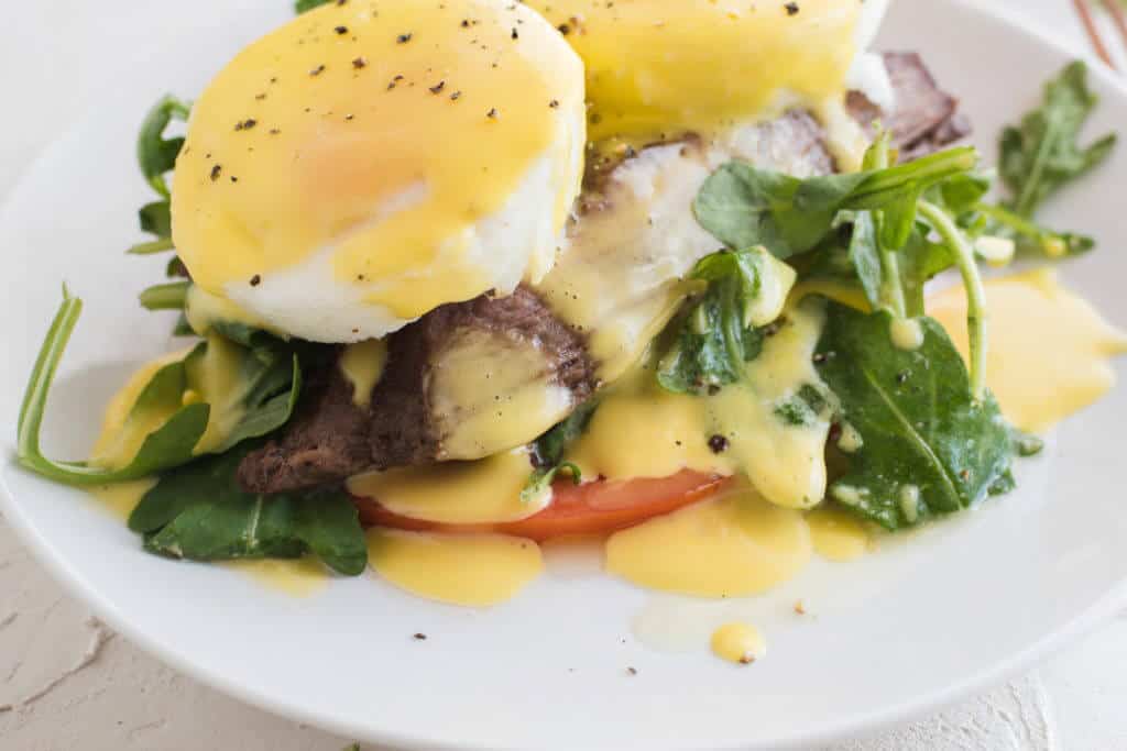 Close-up of Steak Eggs Benedict covered in Lemon Vinaigrette on a plate. 