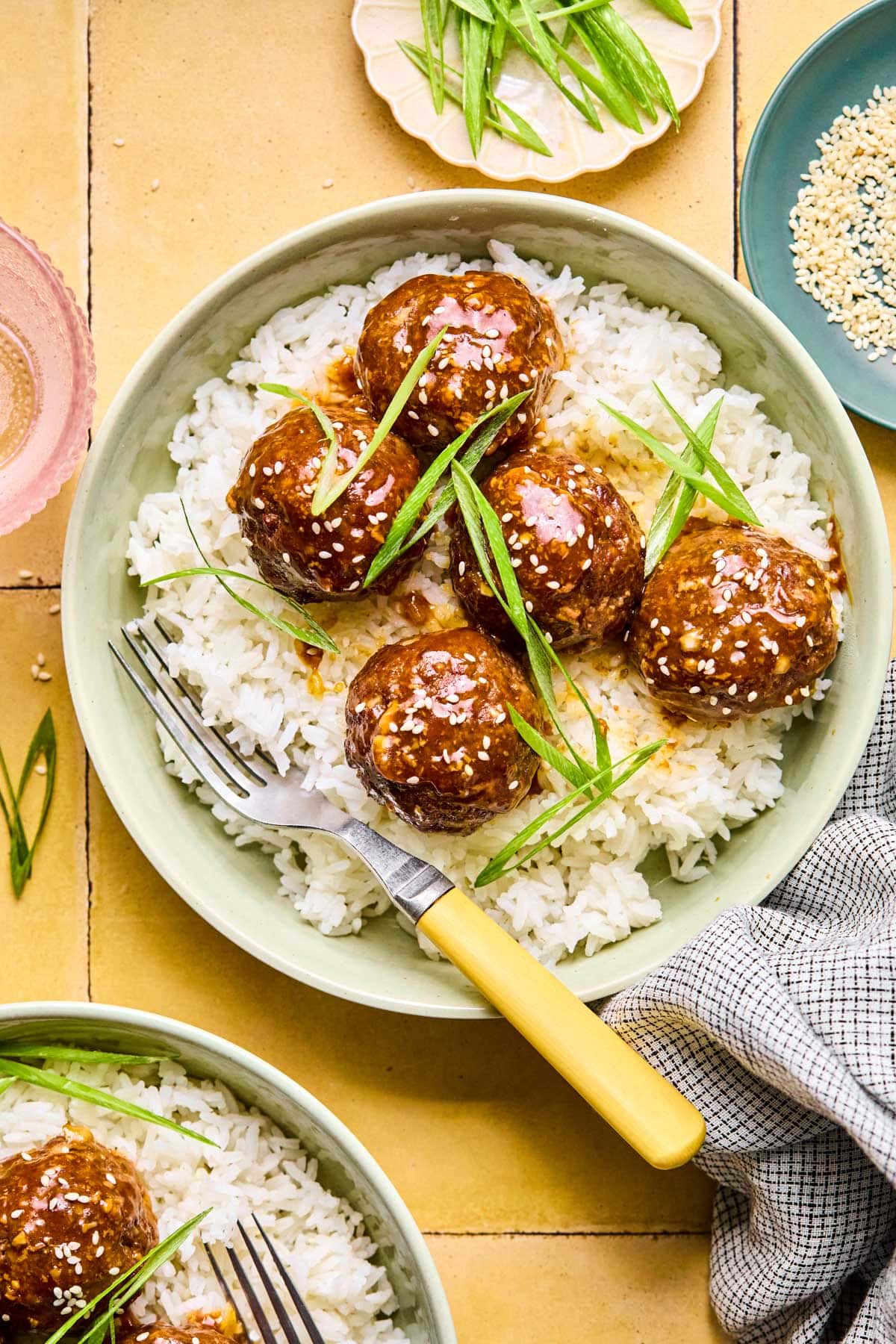 Asian meatballs in a green bowl garnished with green onions and sesame seeds laid over a bed of rice.