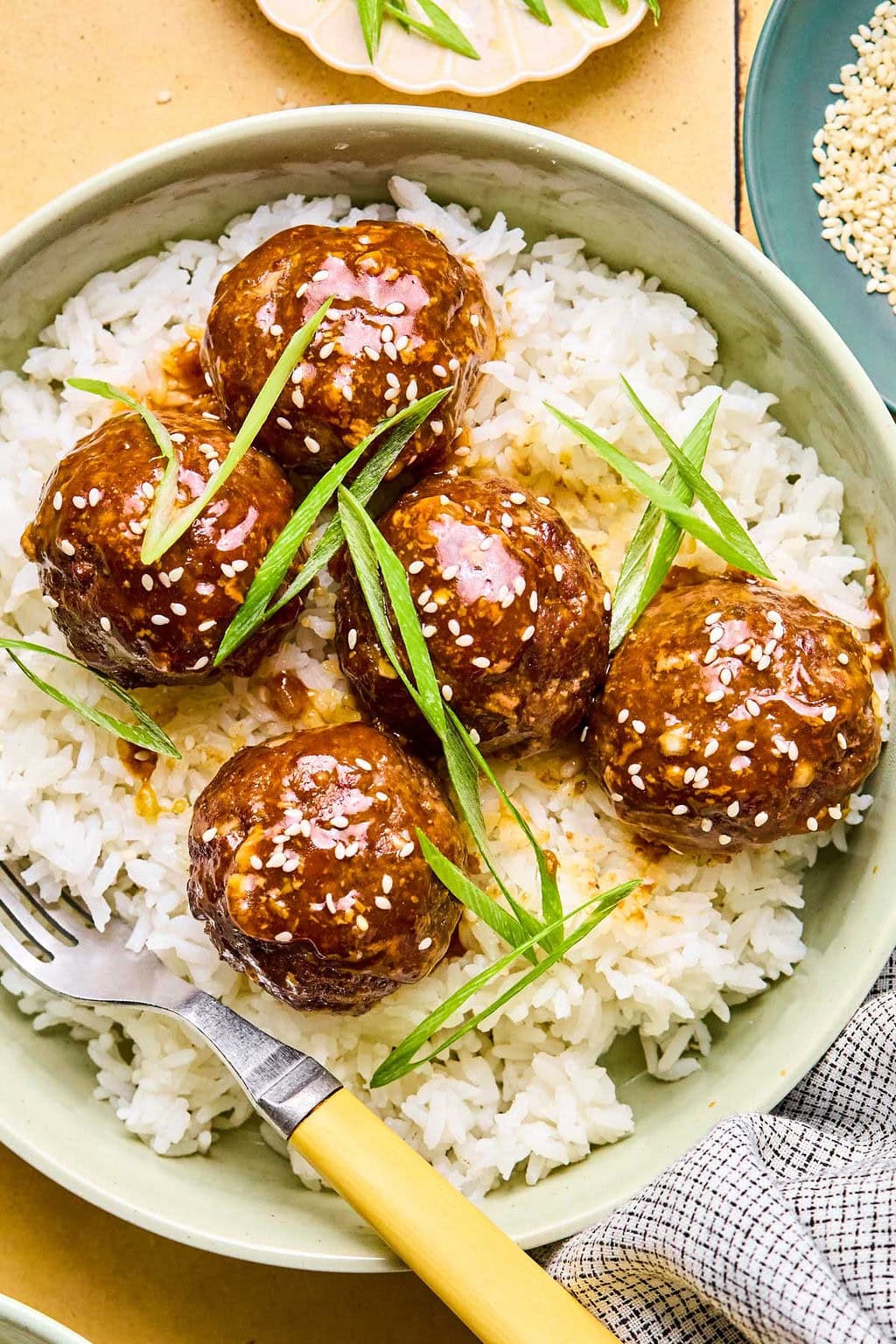 Asian meatballs coated in a sticky sauce garnished with green onions and sesame seeds over a bed of rice.