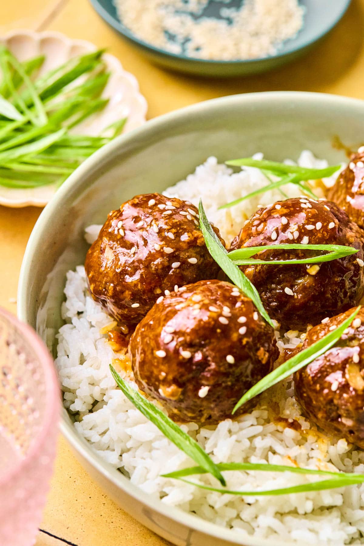 A green bowl of Asian meatballs garnished with green onions and sesame seeds over a bed of rice.