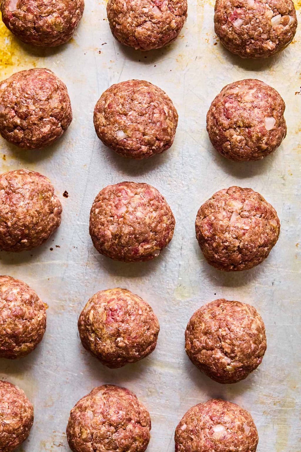 Meatball mixture rolled into golf-ball sized meatballs arranged on a sheet pan.