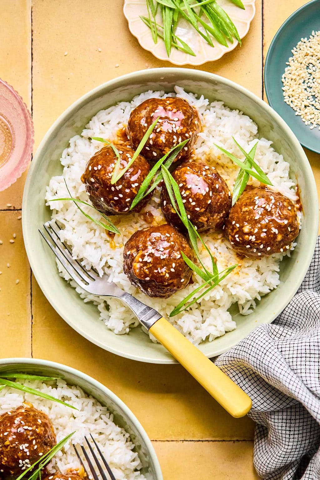 Asian meatballs in a green bowl garnished with green onions and sesame seeds laid over a bed of rice.