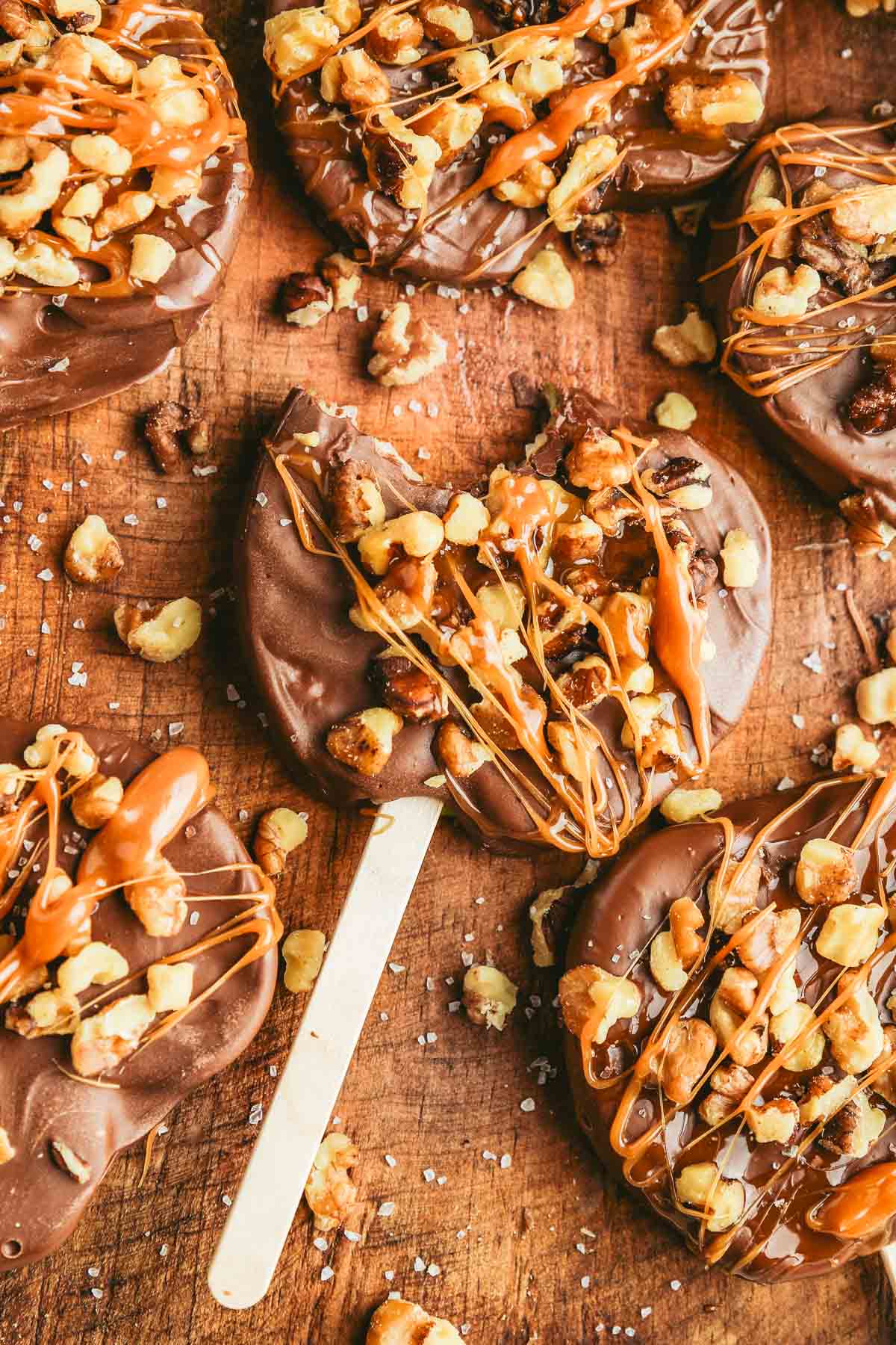 apple slices on a popsicle stick garnished with chocolate, caramel, walnuts and sea salt. 