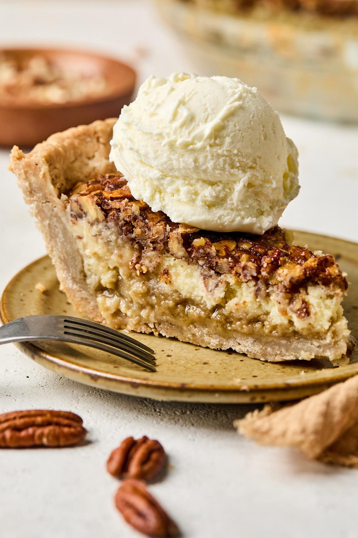 a slice of creamy pecan pie topped with a scoop of vanilla ice cream. 