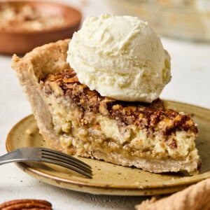 a slice of creamy pecan pie topped with a scoop of vanilla ice cream.