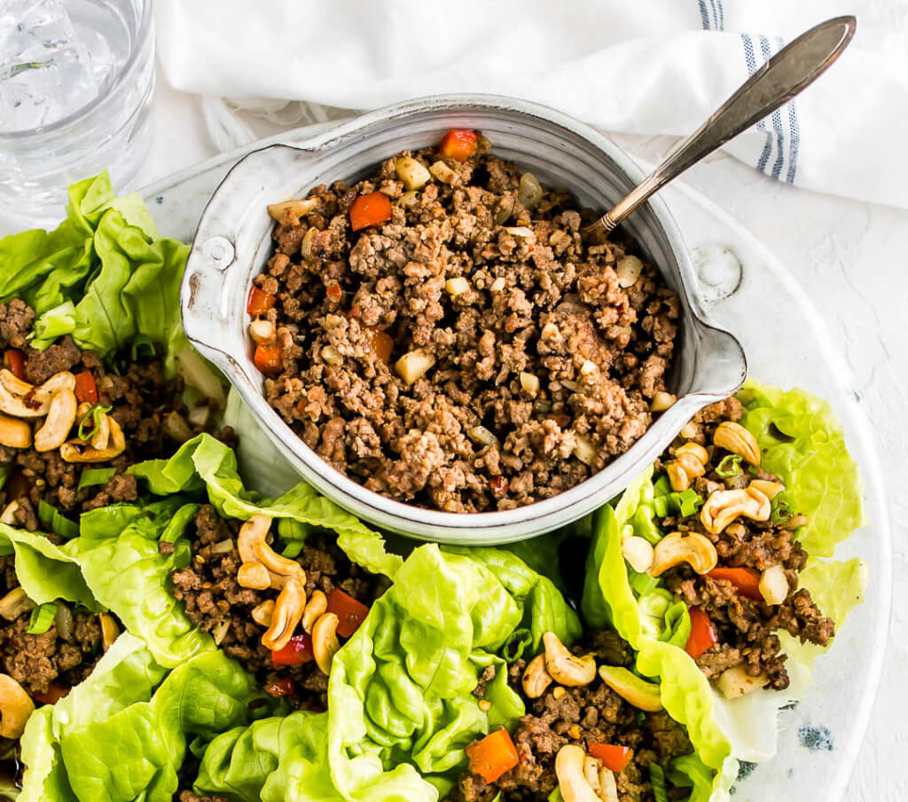 ground beef lettuce wraps on a white plate next to a bowl of Asian-inspired ground beef filling. 