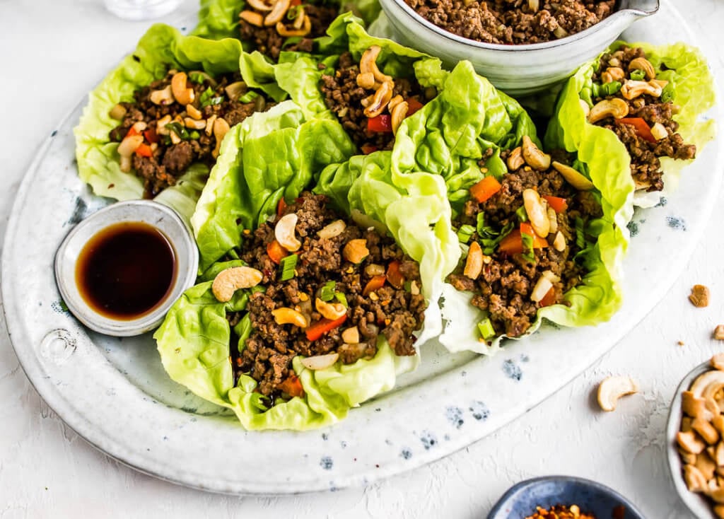 a batch of lettuce wraps on a white place with ground beef and sauce.