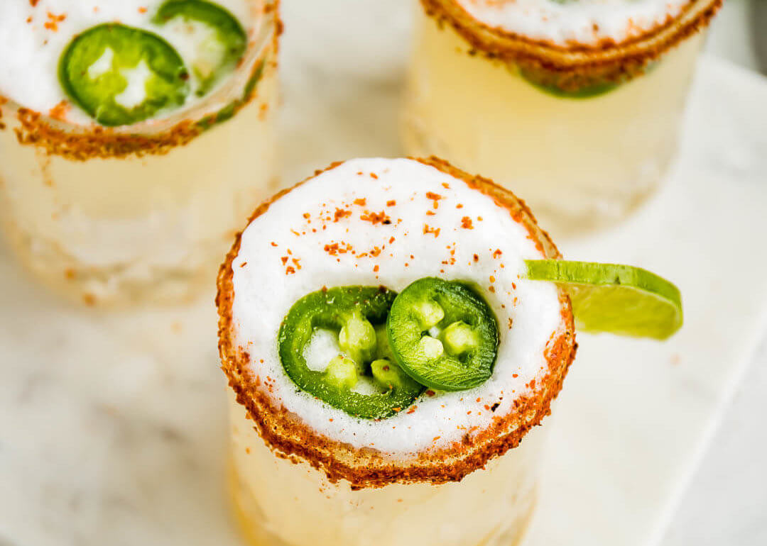 glass filled with spicy margarita with a tajin seasoned rim and fresh jalapeno slices and lime wedge for garnish