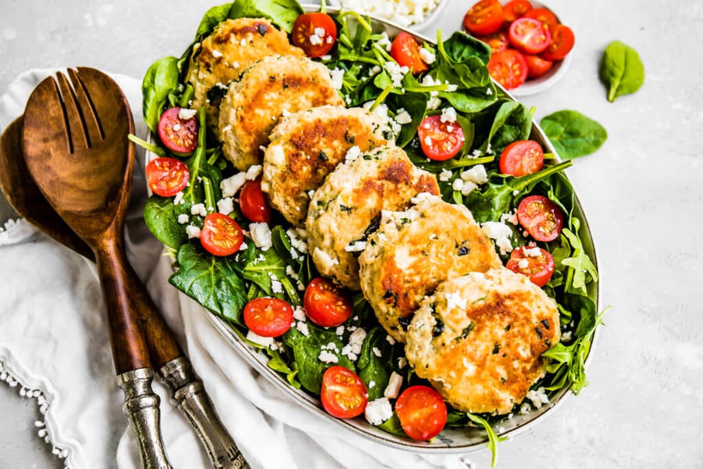 macro friendly Chicken Feta Burger Patties on a bed of spinach.