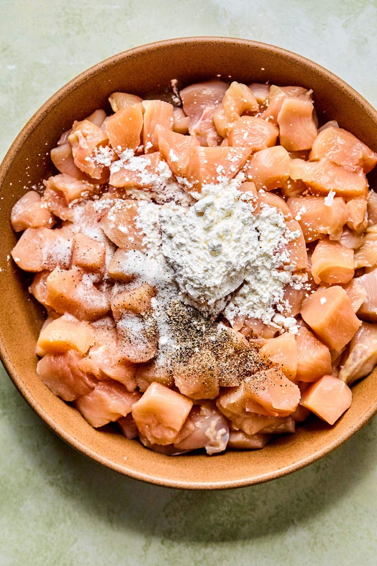 Raw chicken pieces tossed with arrowroot, salt, and pepper in a mixing bowl.