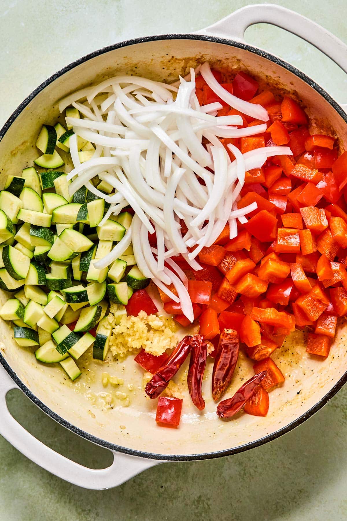 Bell peppers, onion, zucchini, garlic, and dried chilies ready to stir fry in a skillet.