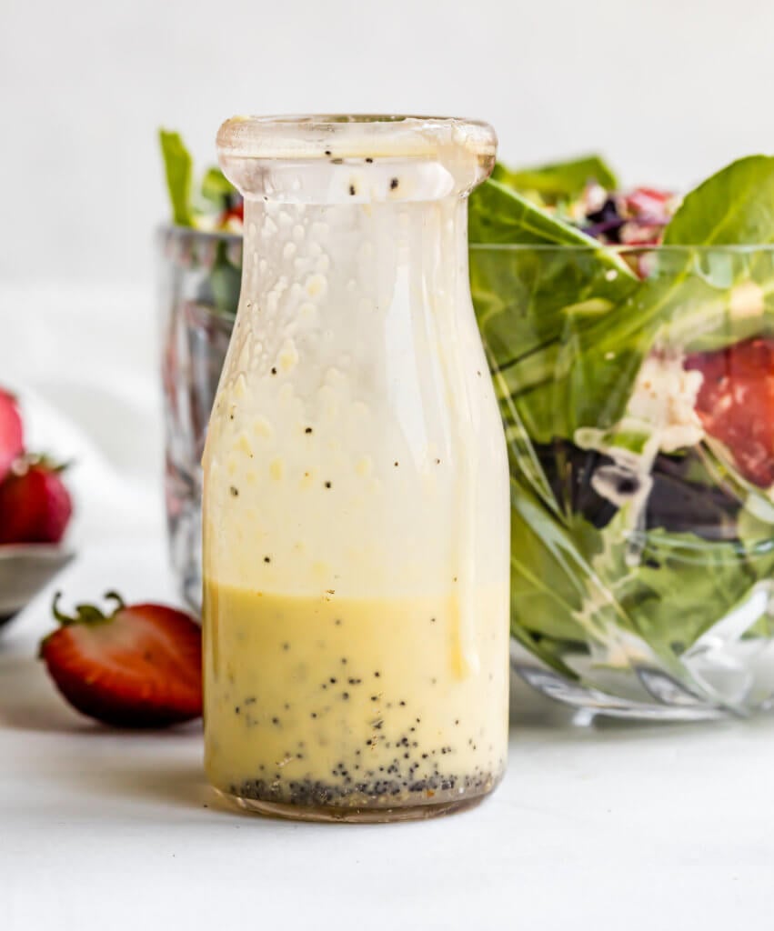 a jar of poppy seed dressing by greens.