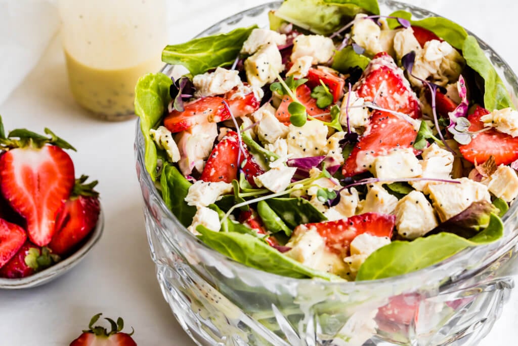 a bowl with lettuce, chicken and red onions drizzled with poppy seed dressing. 