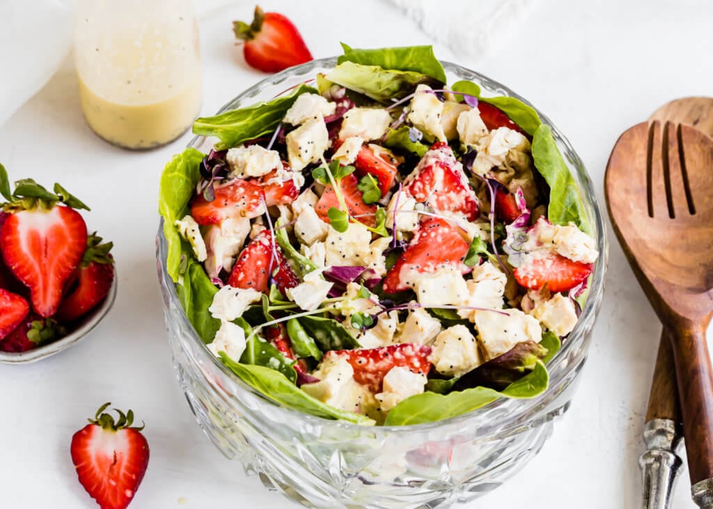 a bowl with lettuce, chicken and red onions drizzled with poppy seed dressing. 