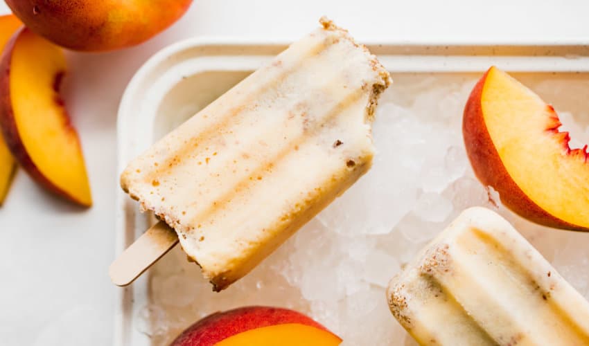 Peach Crisp Popsicles on ice with sliced peaches