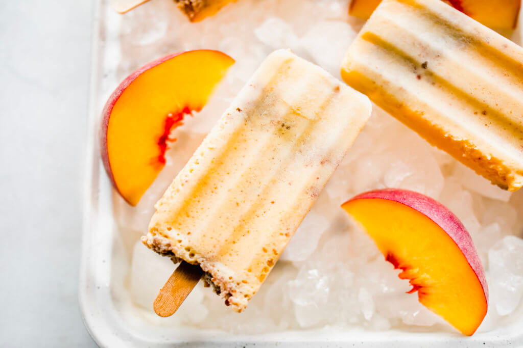 Peach popsicles on a tray with ice and sliced peaches