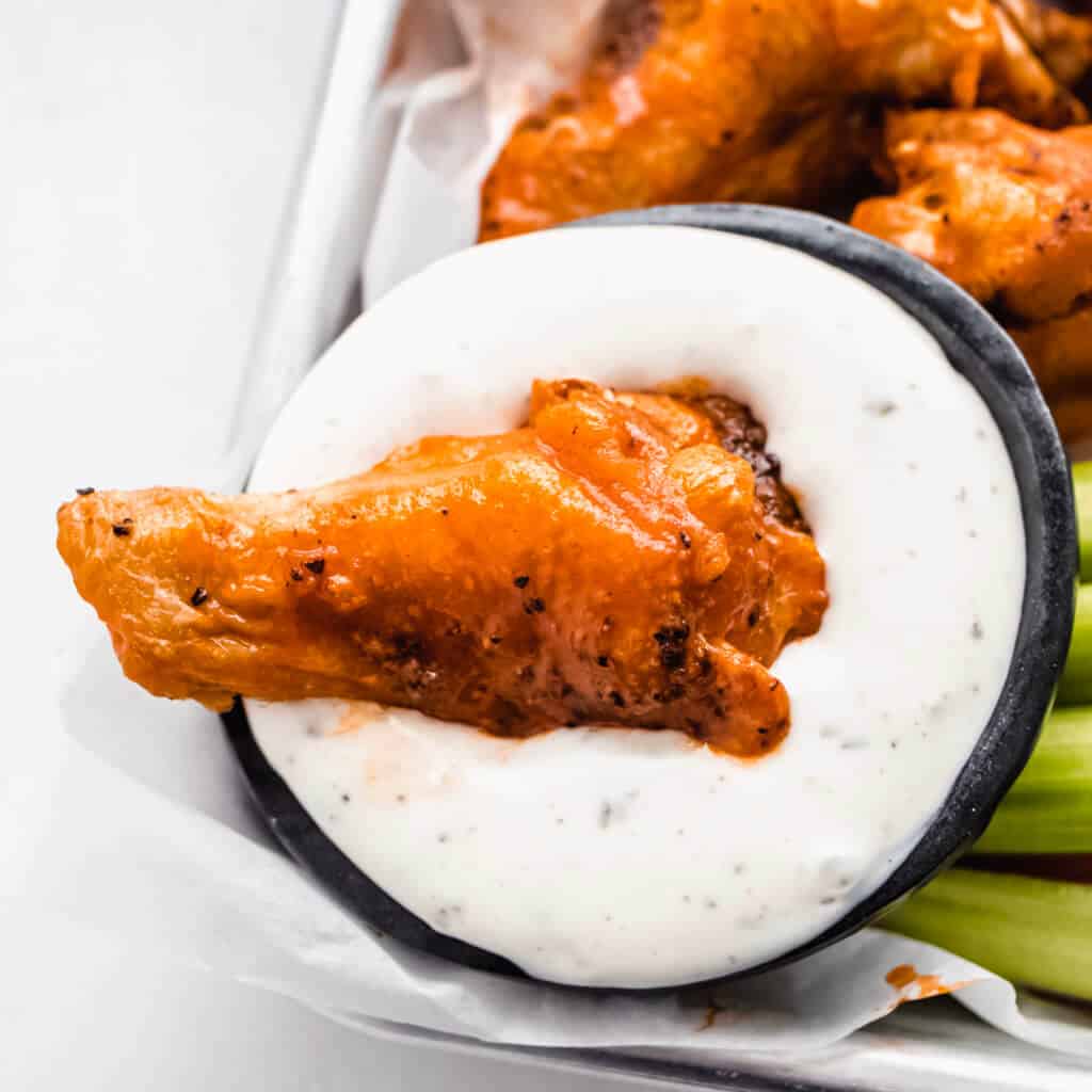 A close up image of a chicken wing drenched in ranch dressing. 