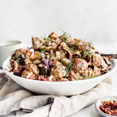 Potato salad in a white bowl with bacon, ranch, red onion and fresh dill.