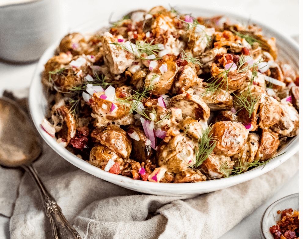 Potato salad in a white bowl with bacon, ranch, red onion and fresh dill. 