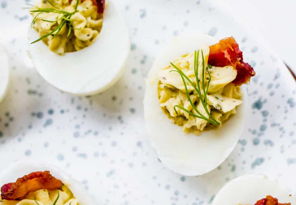 A closeup picture of a deviled egg garnished with fresh dill and topped with crispy bacon.