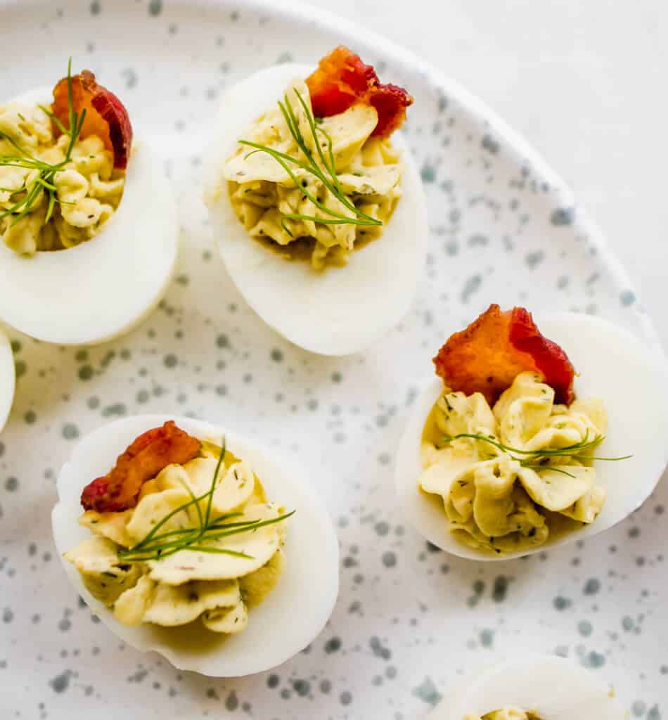 A platter of bacon ranch deviled eggs garnished with fresh dill and crispy bacon