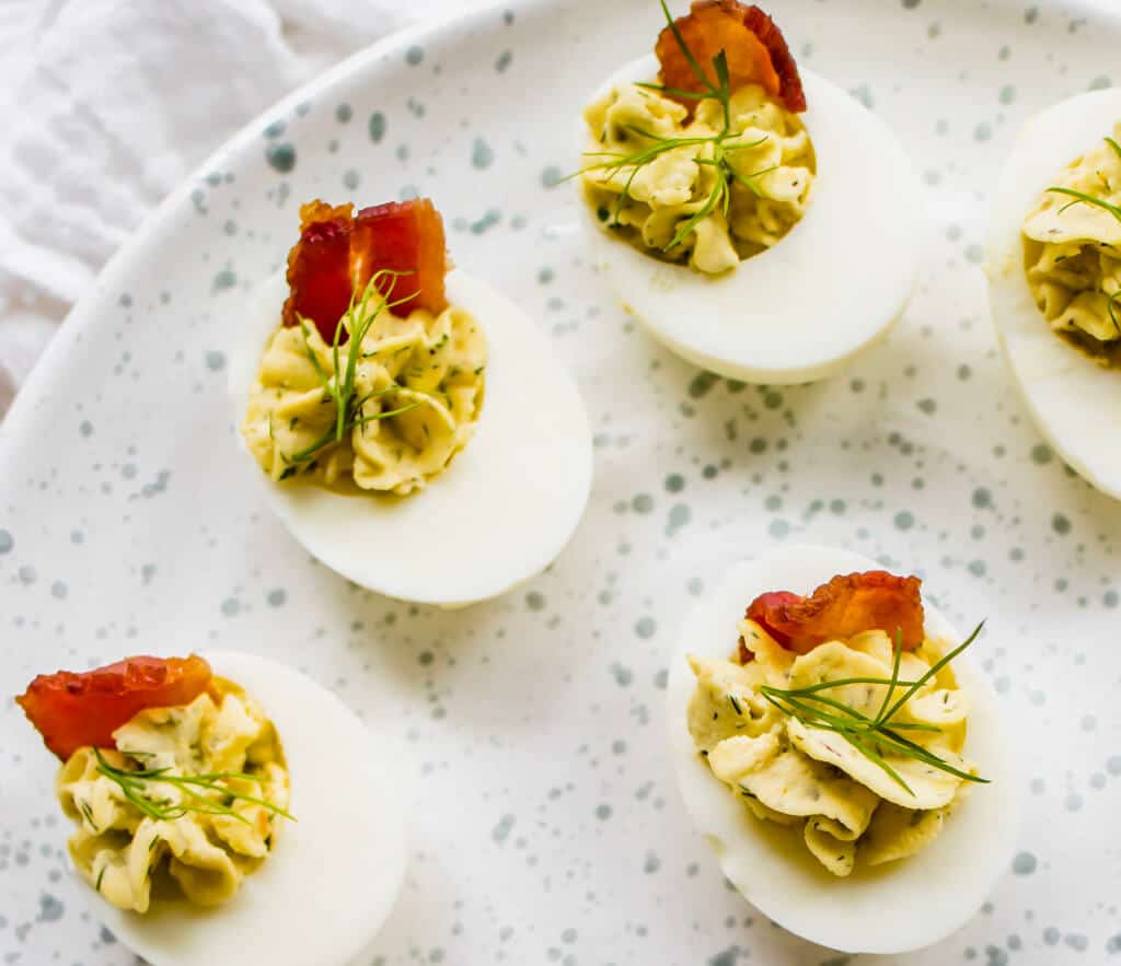 A platter of deviled eggs garnished with fresh dill and crispy bacon