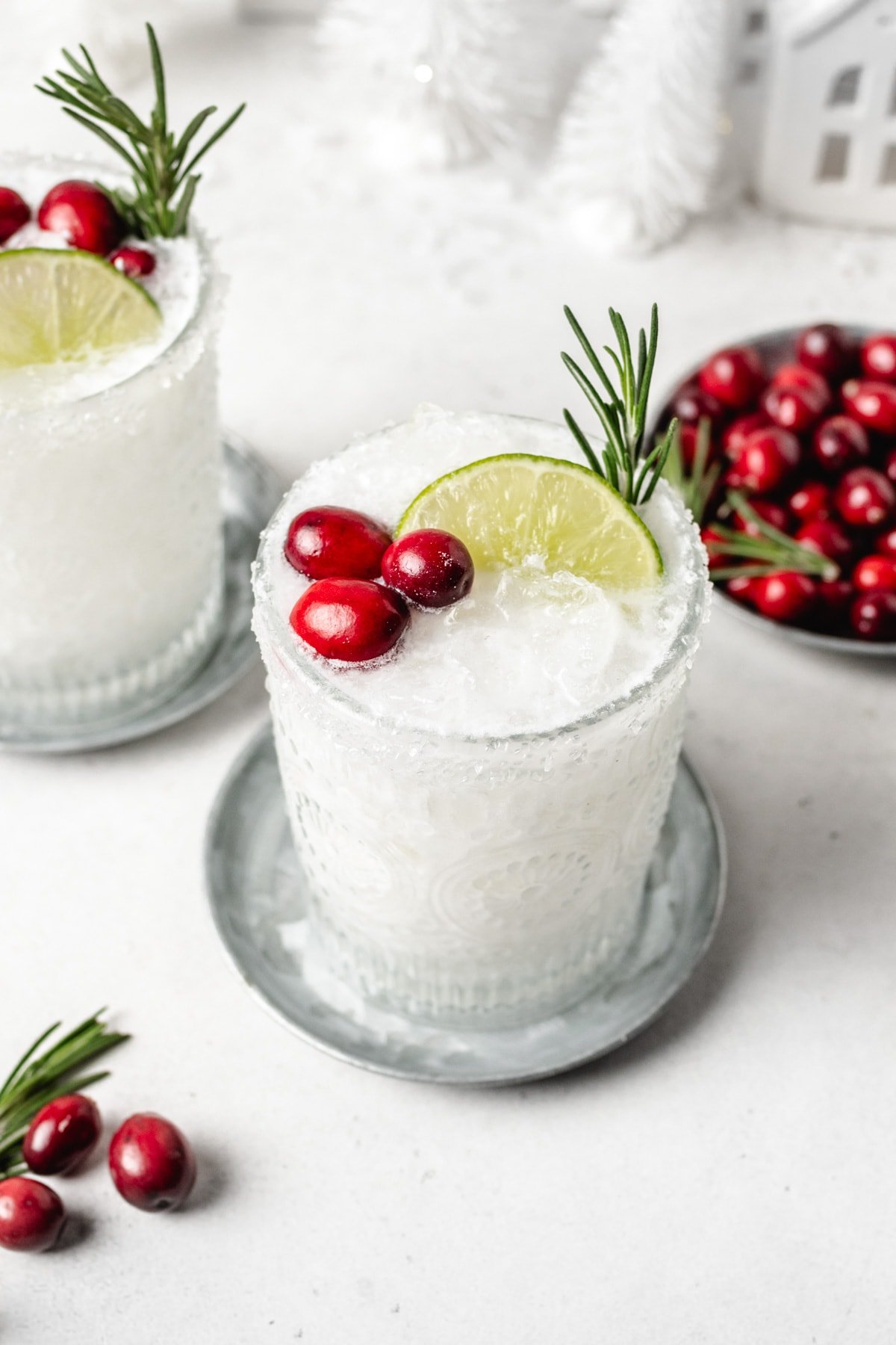 a glass filled with white christmas margarita and topped with cranberries, lime, and rosemary