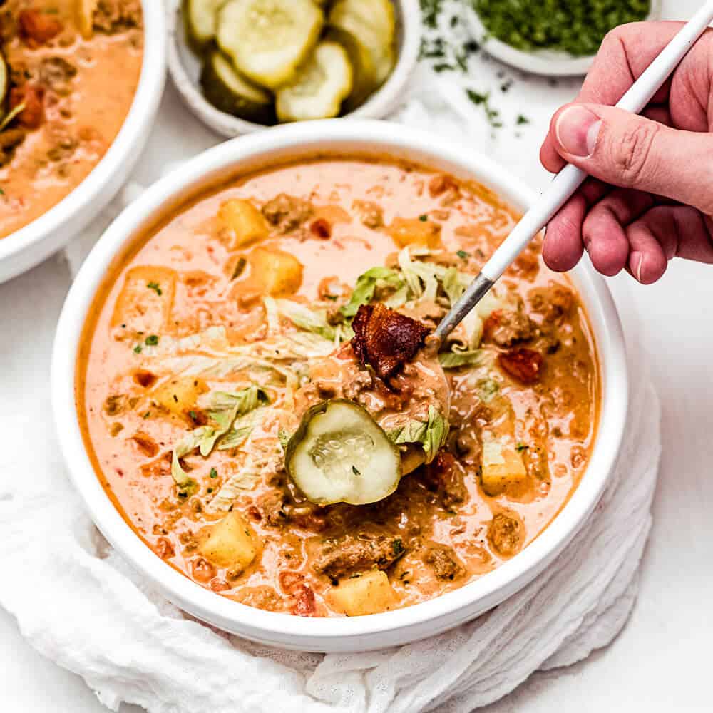 A close up photo of the soup topped with a pickle and slice of bacon