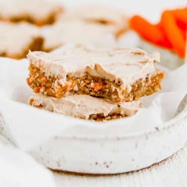 a stack of carrot cake bars in a white bowl with a bite taken out of the top one