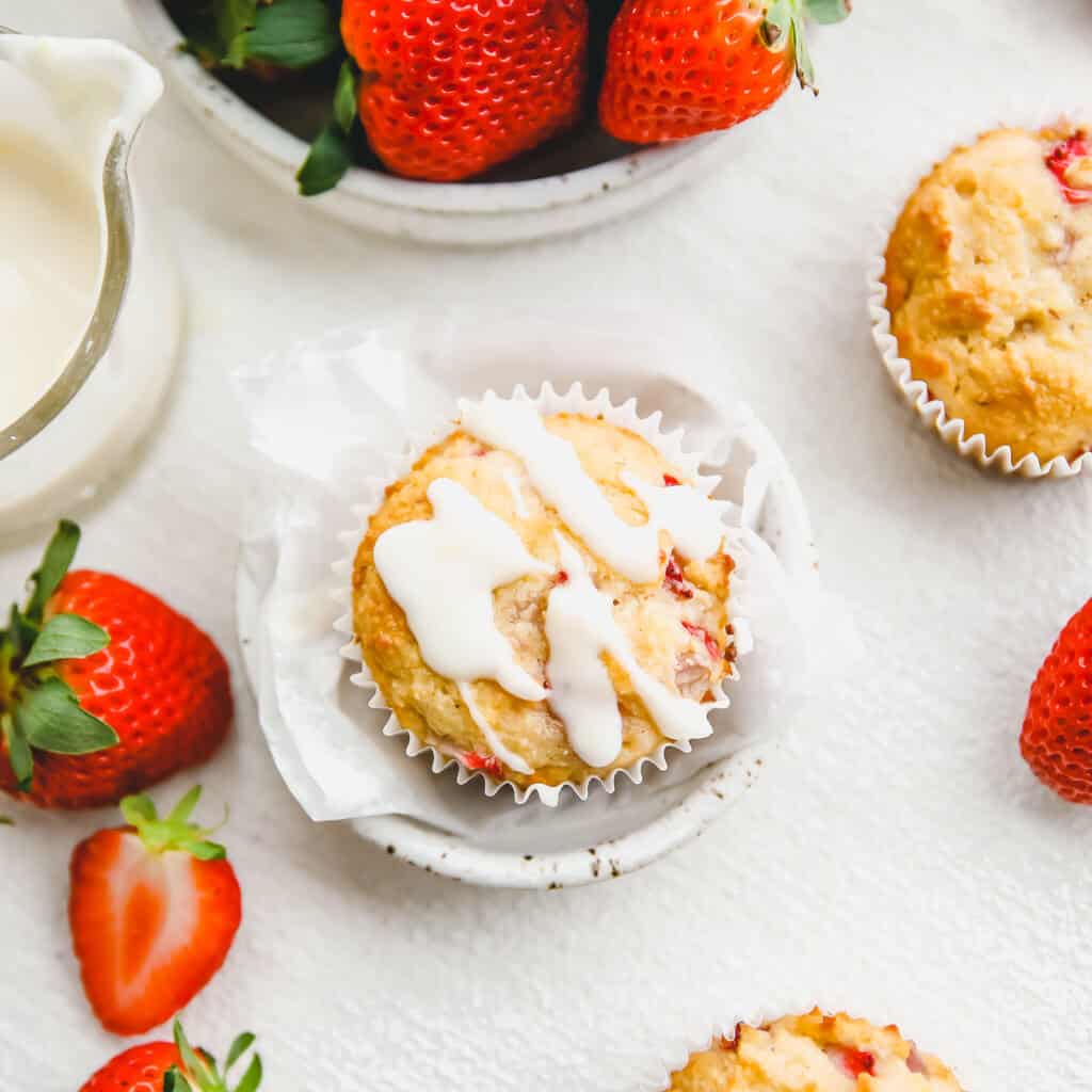 A single muffin on a plate with a white glaze over the top with strawberries for garnish