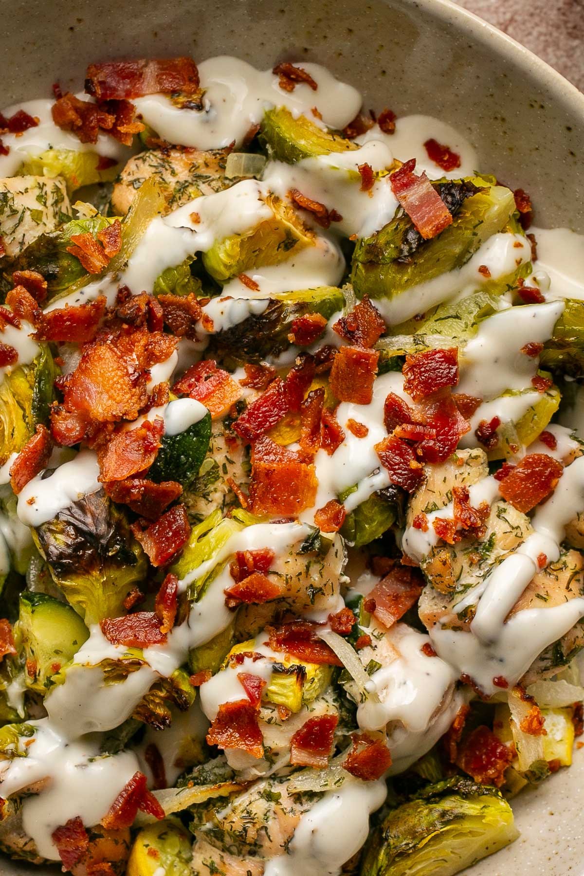 an up close shot of ranch dressing drizzled on top of chicken and veggies with chopped bacon on top