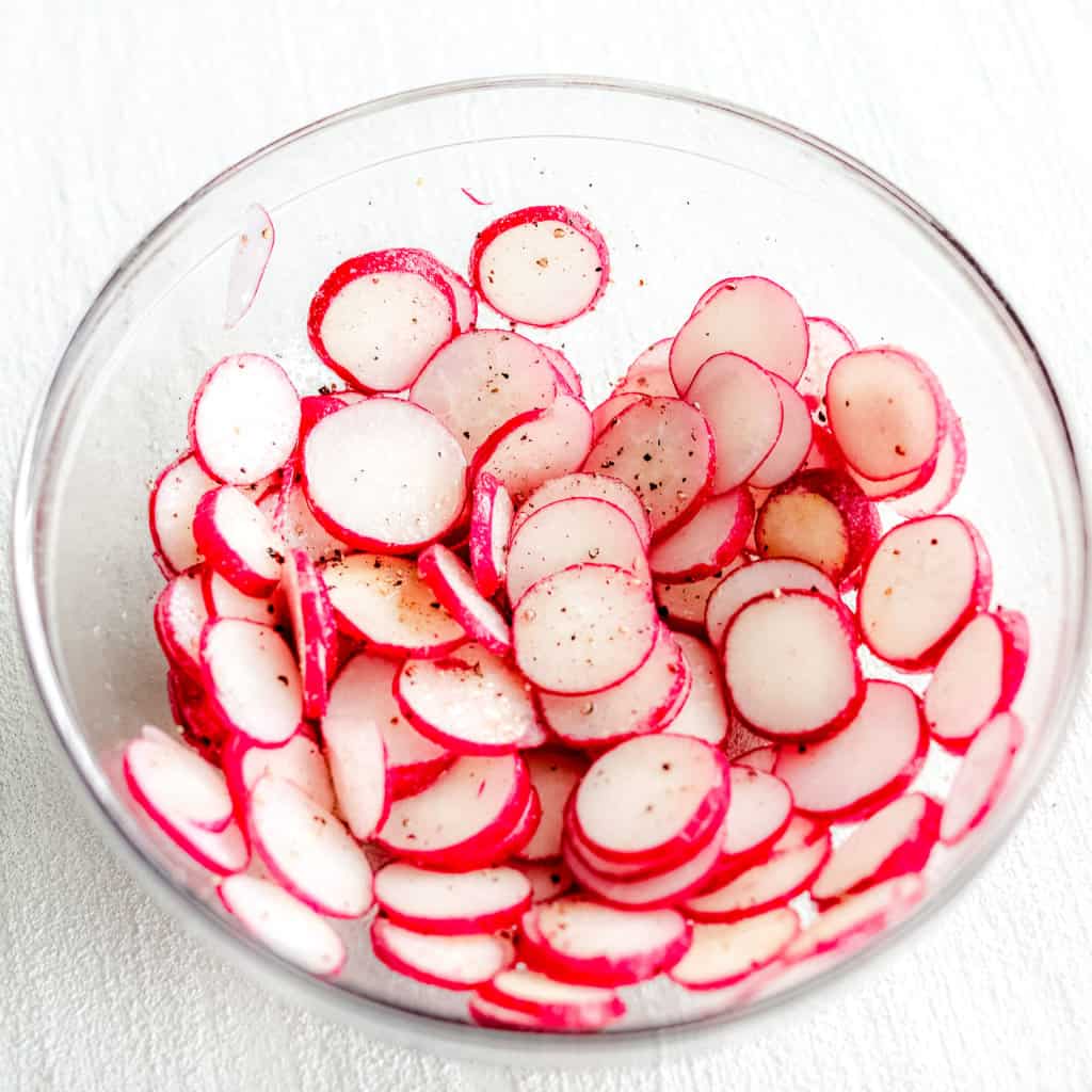 Air Fryer Radish Chips in a bowl with the olive oil, salt, pepper and garlic. 