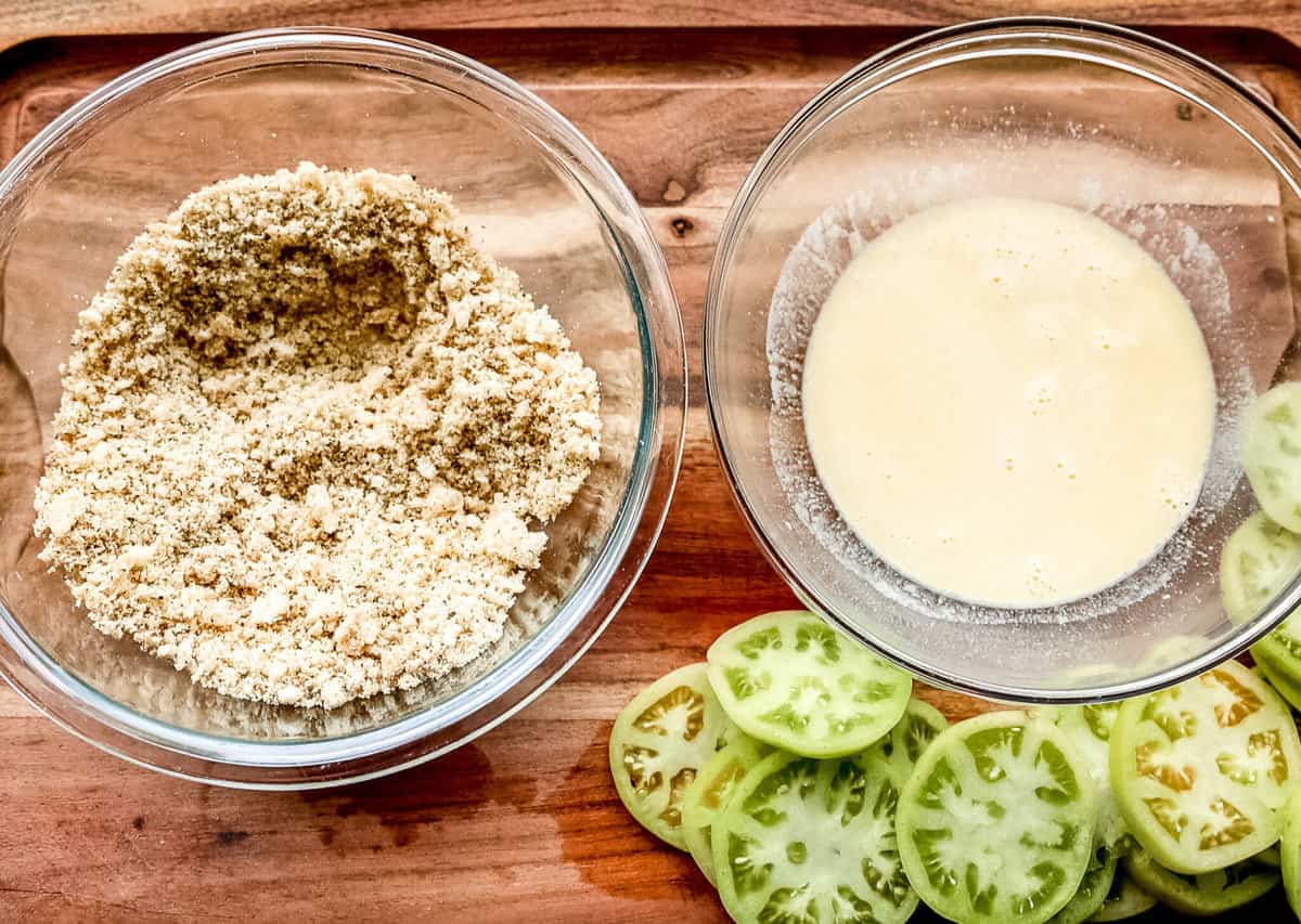 Keto fried green tomatoes recipe ingredients laid out in small bowls on a wooden countertop.