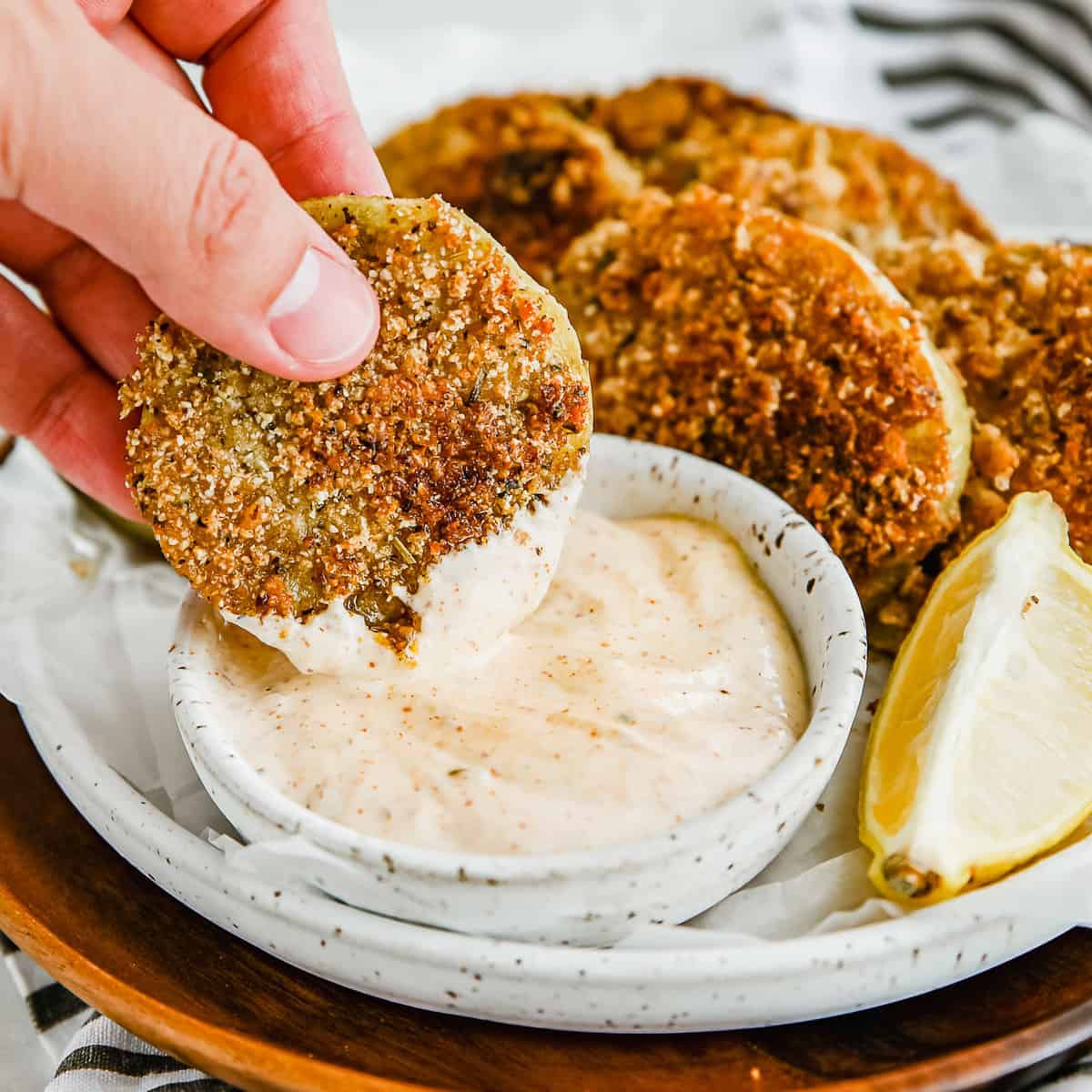 A hand dipping a keto fried green tomato into the zesty dipping sauce.