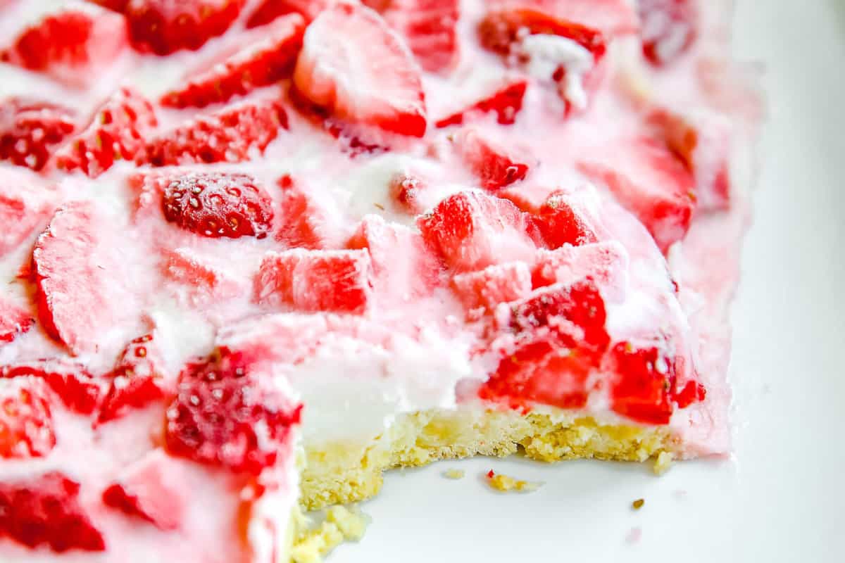 A close up photo of the frozen shortbread with icing and strawberries in a baking dish