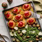 sheet pan meatloaf topped with ketchup next to cooked veggies