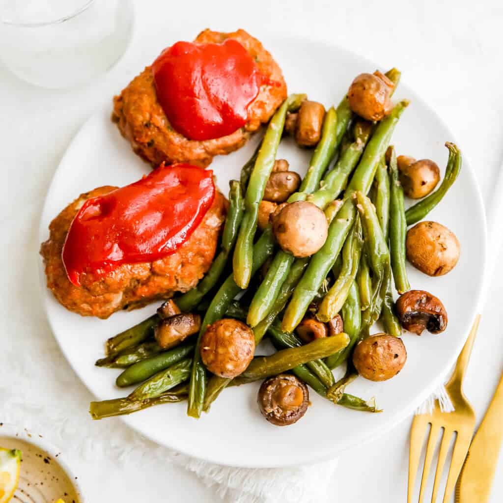 Meatloaves on a sheet pan with green beans and mushrooms on a white plate
