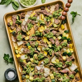 a sheet pan filled with steak and vegetables and covered in chimichurri sauce