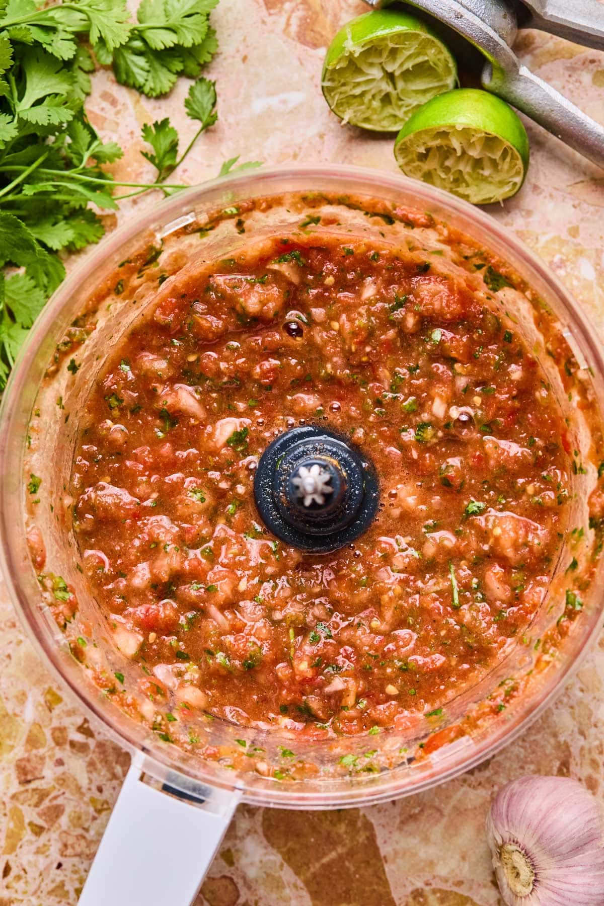 Food processor filled with fresh salsa ingredients - tomatoes, onion, cilantro, jalapeño, and lime after blending.