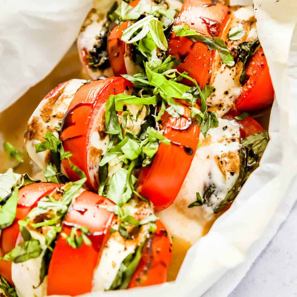 A close up photo of a stuffed tomato with melted cheese, basil and pesto.