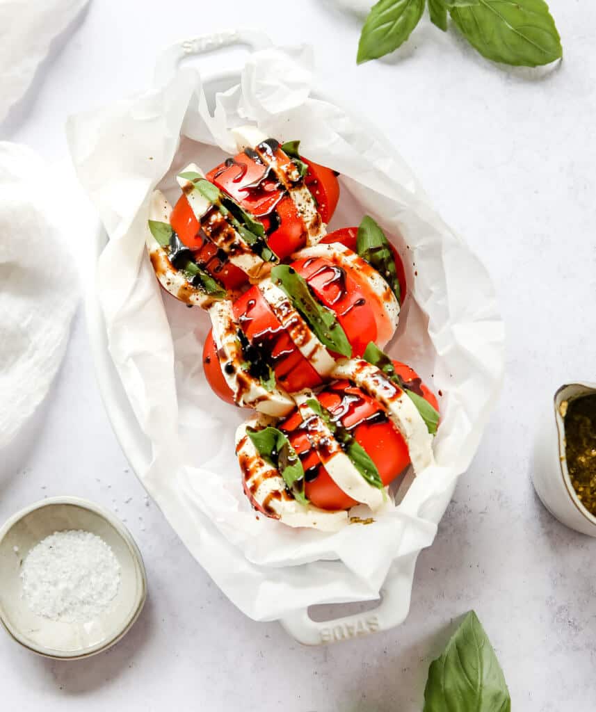 A overhead shot of 3 roma tomatoes stuffed with cheese, basil and topped with olive oil, balsamic reduction, salt and pepper