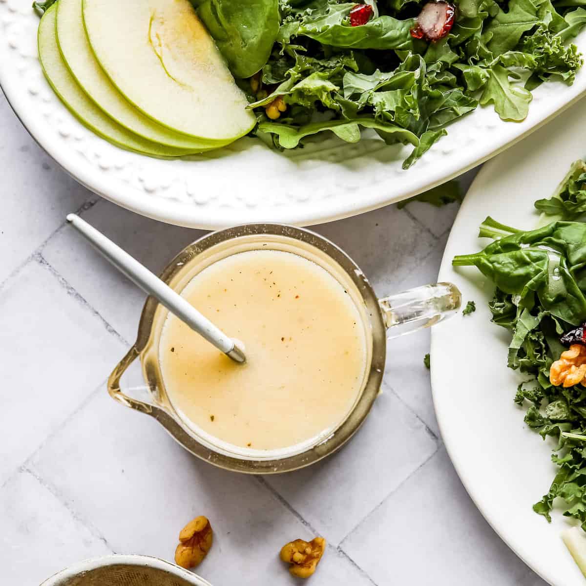 Harvest Chicken Apple Salad on two white plates and a glass jar filled with Honey Lemon Vinaigrette and a spoon with a white background