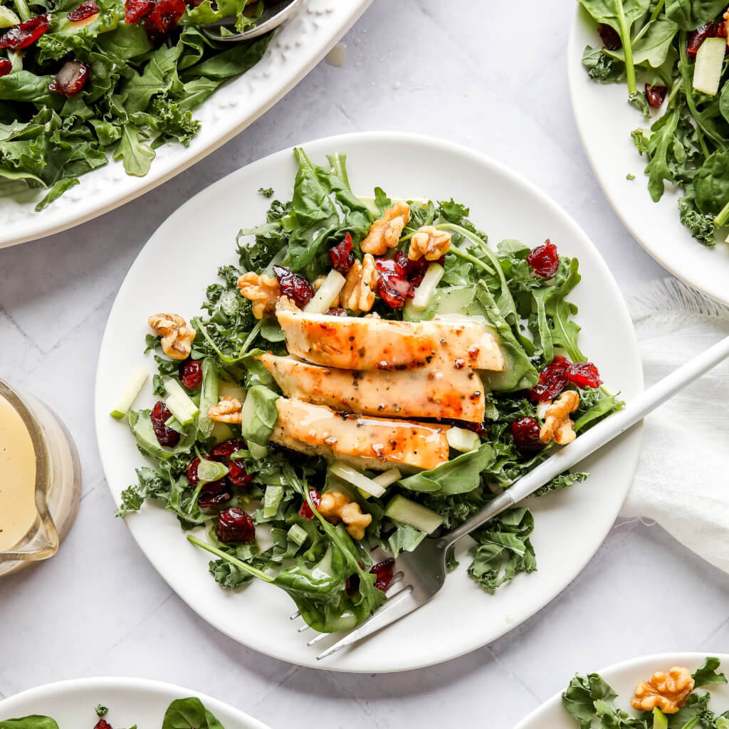 Harvest Chicken Apple Salads on five white plates and a glass jar filled with Honey Lemon Vinaigrette and a spoon on a white background