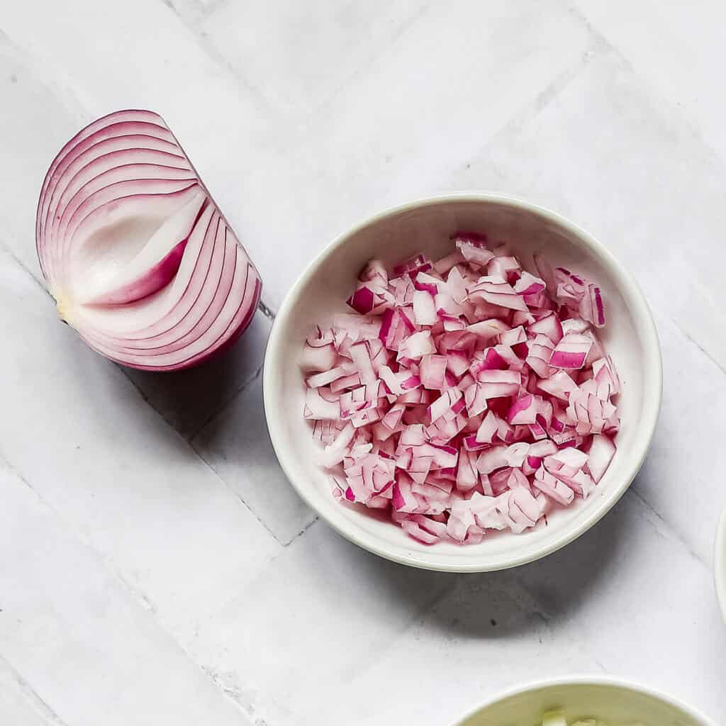 half of a red onion next to diced red onion in a white bowl with a white background