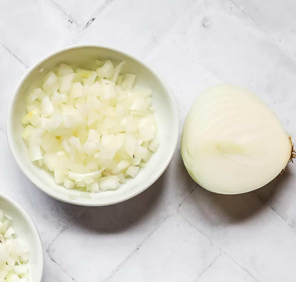 half of a vidalia onion next to diced vidalia onion in a white bowl with a white background