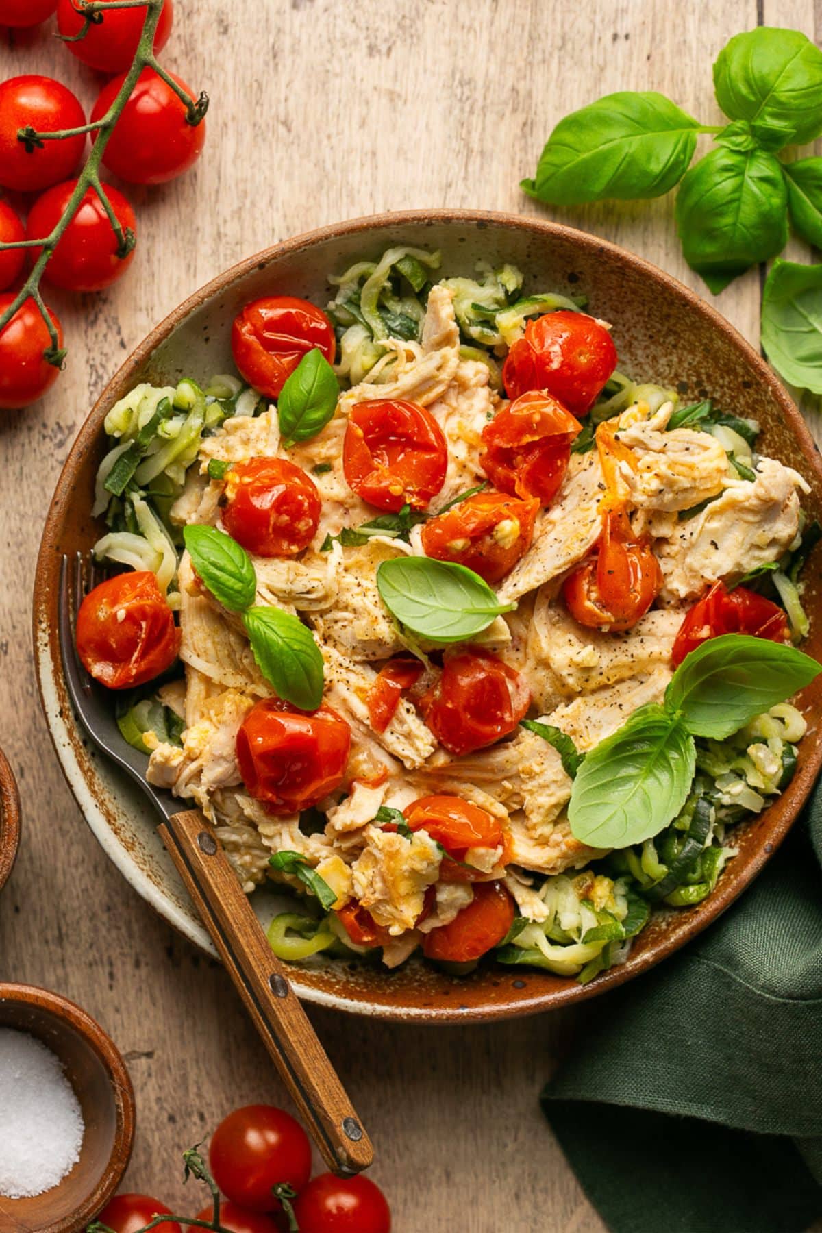 an overhead shot of chicken and tomato bake in a brown bowl topped with fresh basil 