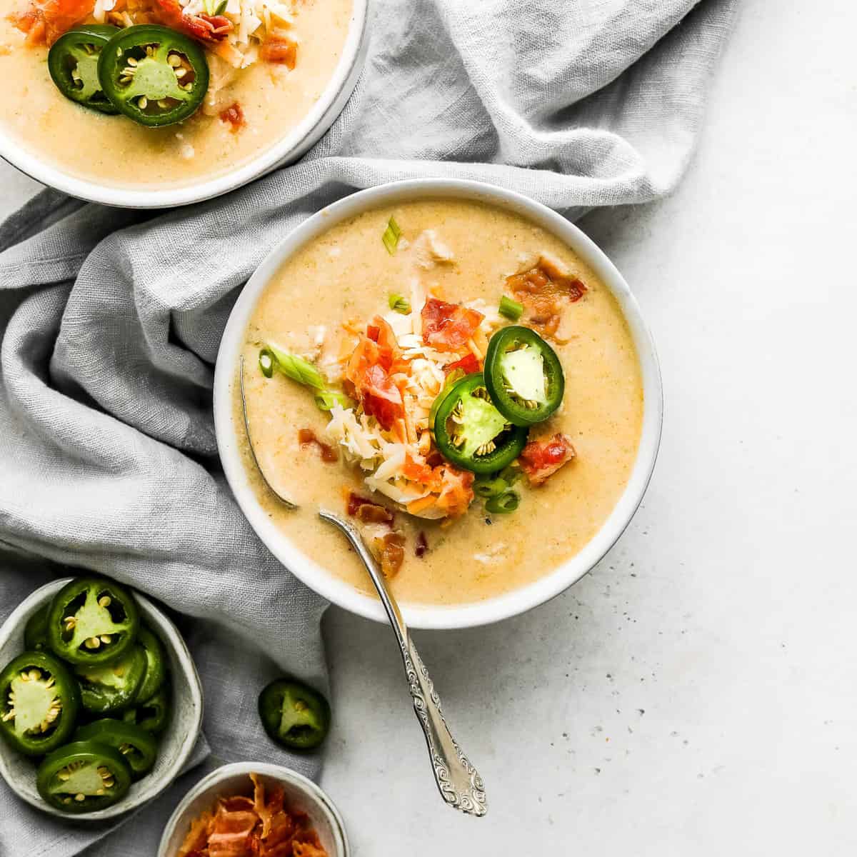 keto jalapeno popper chicken soup in a white bowl with a spoon resting on the side. 