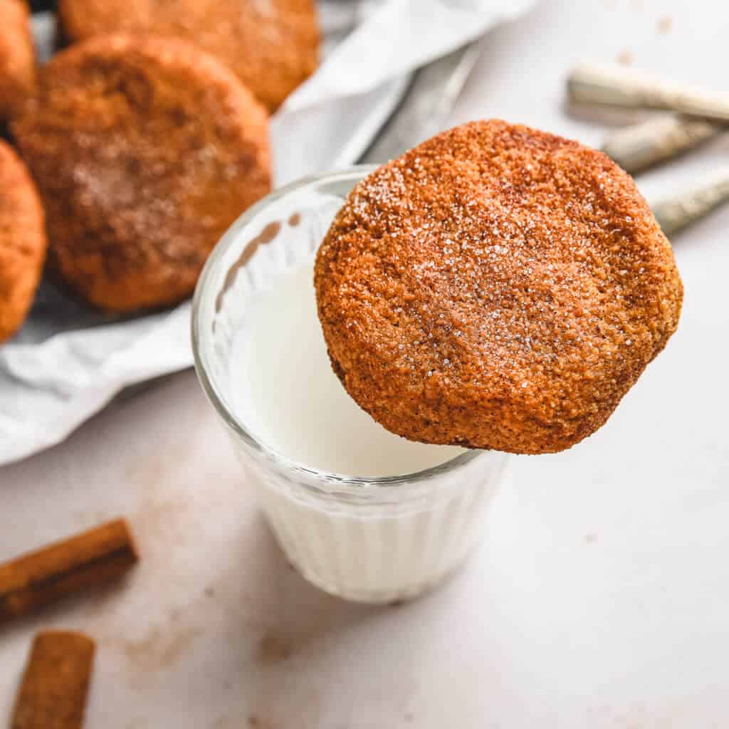keto pumpkin snickerdoodle cookie resting on a glass of milk with cinnamon sticks and a white background