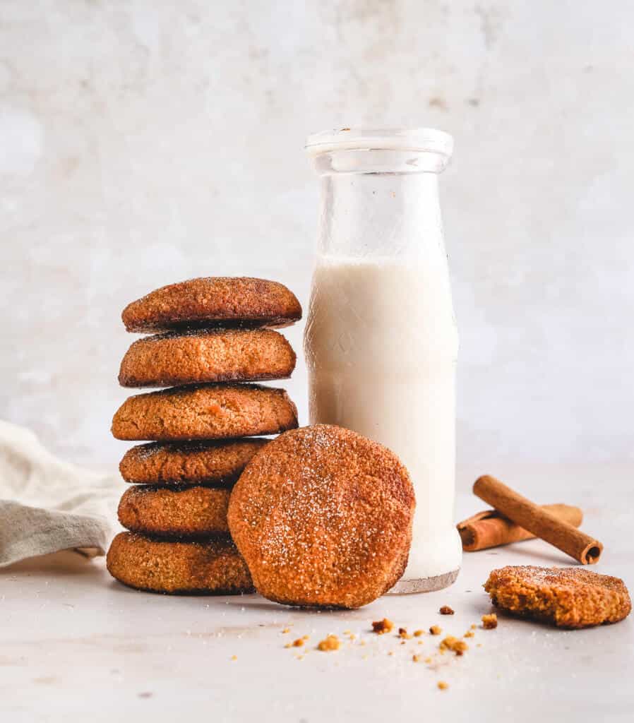 keto pumpkin snickerdoodle cookies stacked next to a glass bottle of milk with cinnamon sticks and a white background